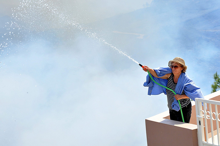 Wildfires Greek islands: A woman uses a garden hose to protect her house from a fire near Istrion vi