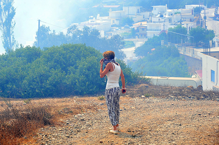 Wildfires Greek islands: A woman covers her face to protect it from smoke from a fire that broke out
