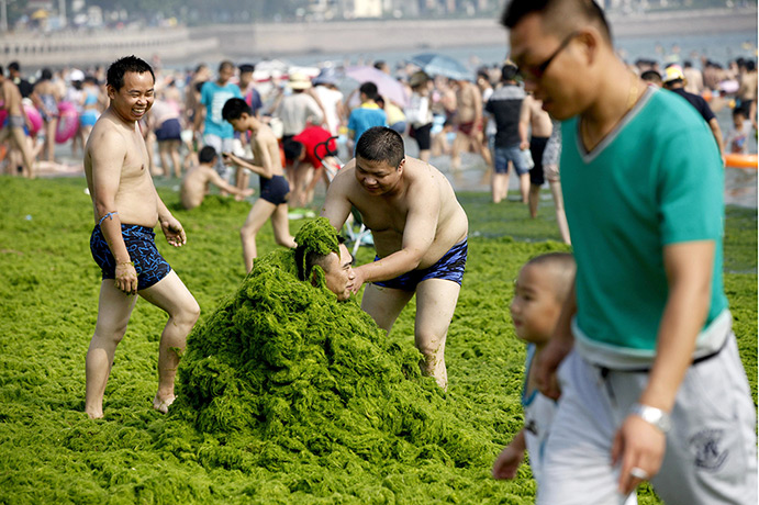 China algae: Tourists have fun on a beach coverign each other