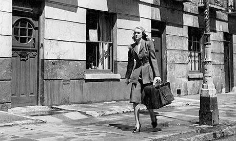 Black and white shot of woman walking down the street with suitcase