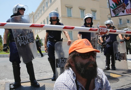 A municipal worker sits in front of riot police guarding the parliament during a rally against public sector reforms in Athens July 9, 2013.