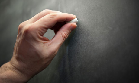 A man male teacher left hand writes using chalk on a chalkboard blackboard.