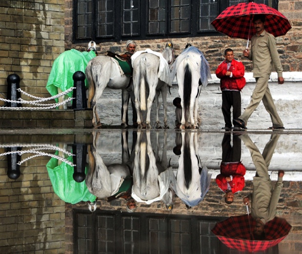 The reflection of horses, their keepers, and an umbrella-toting pedestrian is seen in a puddle of water following heavy monsoon rains in the northern hilltown of Shimla, India. The monsoon, which covers the subcontinent from June to September and usually brings flooding, accounts for about 80% of India's annual rainfall