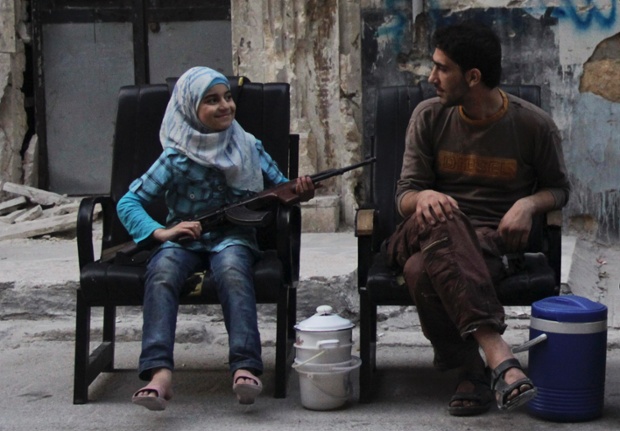 A girl holds a gun across her lap, as she sits with a Free Syrian Army fighter along a street in Aleppo.