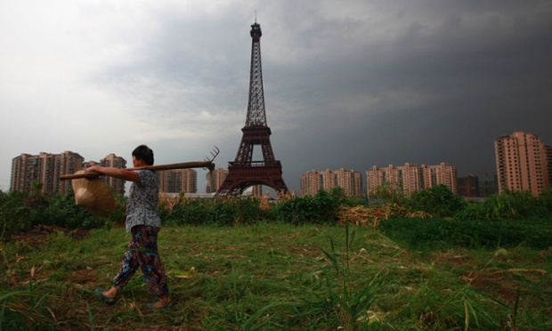 The Eiffel Tower relocates to China. A farmer carrying a rake walks down a dirt road past a replica of the Eiffel Tower at the Tianducheng development in Hangzhou, China. Tianducheng began construction in 2007 and was known as a knockoff of Paris with a replica of the Eiffel Tower and Parisian-style houses. Although designed to accommodate at least 10 thousand people, Tianducheng remains sparsely populated and is now considered as a ghost town.