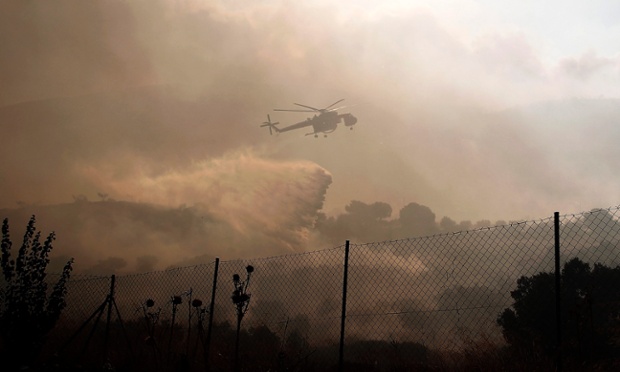 Firemen try to extinguish a fire burning a forest in the area of Markopoulo, Attica region, Greece, using a helicopter. A wildfire that broke out today near the popular seaside resorts of Markopoulo and Porto Rafti in eastern Attica, has reached residential areas.