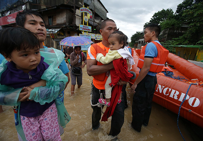 Manila floods: A man and a rescuer carry children to higher grounds as government authorit