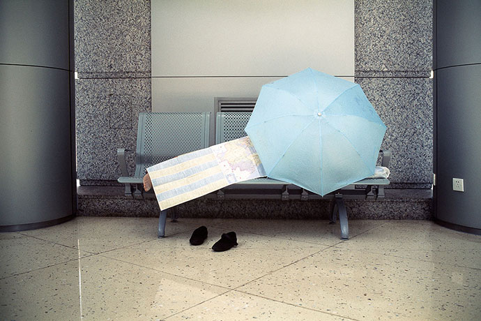 Big Picture - Daydreamers: man lying on bench with blue umbrella covering him
