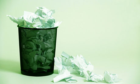 A wastepaper basket with crumpled up paper in it