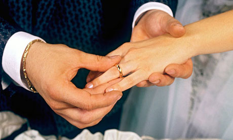 Groom places gold wedding ring on the finger of his new bride in marriage ceremony