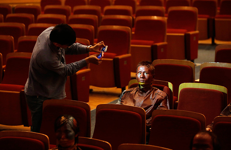 FTA: Jason Lee: A painted participant is lit by two smart phones as an assistant inspects h