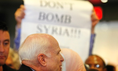 A crowd member holds up signs against military action in Syria  as US Senator John McCain speaks with constituents during a town hall meeting in Phoenix.