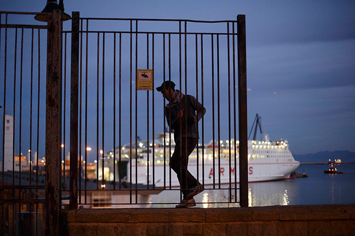 Melilla: A Moroccan youth climbs along a wall overlooking Melilla harbour