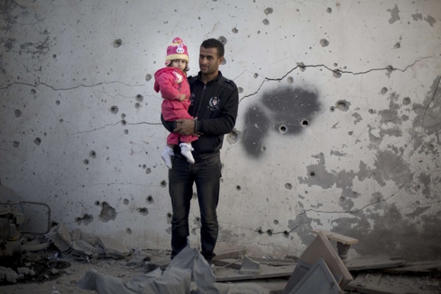 A Palestinian man holds his daughter in front of a damaged building following overnight Israeli air strikes in Gaza City.