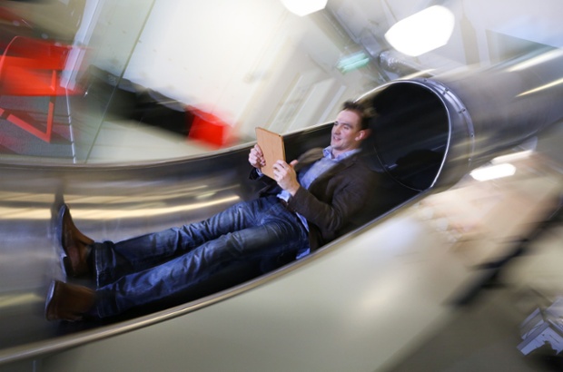 James Avery, manager at the Works in Folkestone, Kent, an innovative business centre, checks his tablet computer as he travels between the floors of the offices using a slide which was installed for staff last summer.