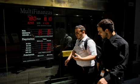 People walk by a sign showing the plunging rate between the Argentine peso and the US dollar in Buenos Aires. The currency has fallen just over 17 percent in the last two days against the dollar, and economic analysts expect inflation to hit 30 percent this year.