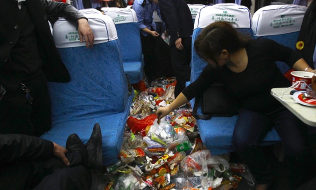 A passenger throws a piece of garbage on the floor as a cleaner collects garbage on a carriage of a train 