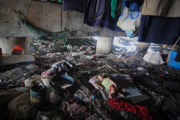 A Filipino boy takes an afternoon rest under a busy bridge used as a shelter in Paranaque, Manila, Philippines.  Between the water below and traffic passing overhead, many Filipino families driven by poverty have set up makeshift residences under bridges.