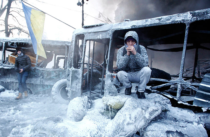 Protests in Ukraine: An anti-government protester sits near a burnt out vehicle in Kiev