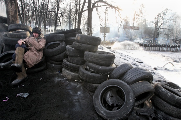 A protester sits behind a barricade of tyres as riot police stand in a line during an anti-government protest during another day of anti-government protests in Kiev.