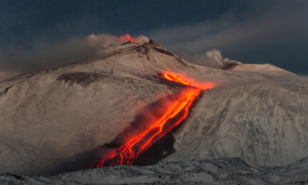 Gas clouds seen atop Mount Etna as red hot lava flows down the snow covered mountainside in Sicily, Italy.