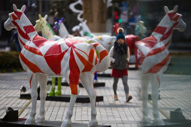 A woman walks past art installations of horses ahead of the upcoming Chinese lunar New Year on a square in Shanghai.