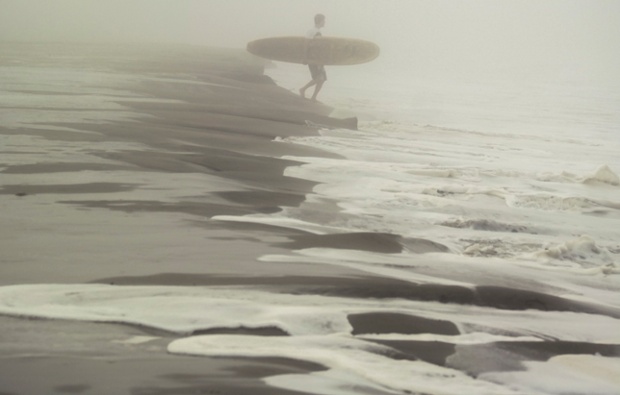Undeterred by the fog, a surfer sets off for a surf session on Venice Beach.