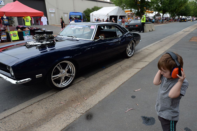 Summernats: A boy wears ear muffs as a car drives by