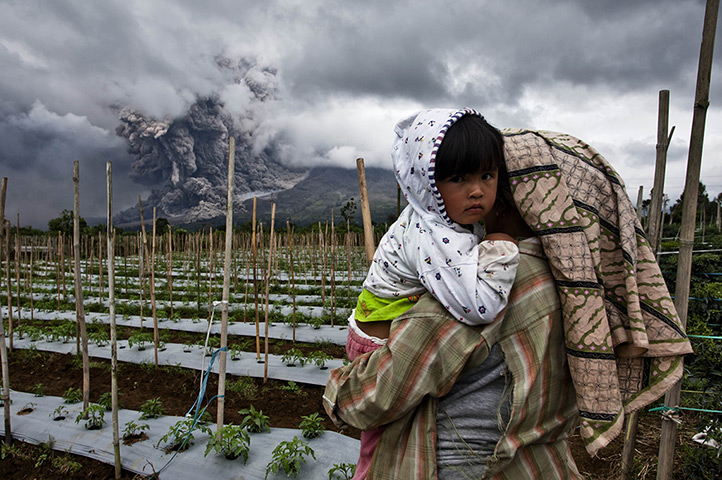 Mount Sinabung: A woman carries her daughter in a nearby field 