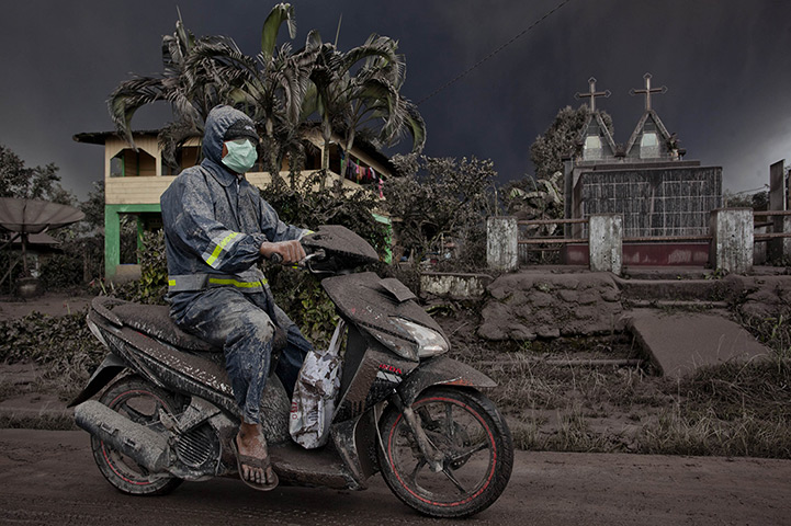 Mount Sinabung: A motorcyclist as drives on a road covered with ash 