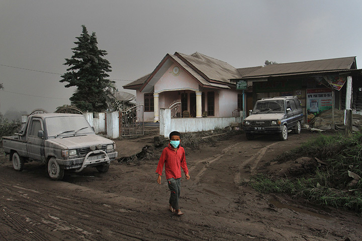 Mount Sinabung: A child stands outside an ash-covered house