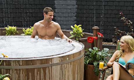 man in a bubbling hot tub smiling at a woman in a bikini on a lounge chair