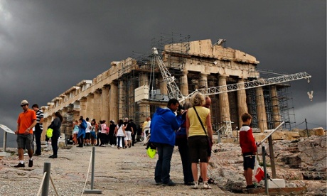 Tourists walk by the Parthenon atop the ancient hill of the Acropolis during a rainy day