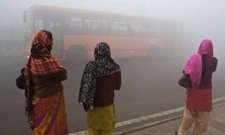 In the city of Delhi, commuters wait for a bus early on a polluted morning.