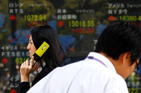 A pedestrian holding her mobile phone walks past an electronic board showing the stock market indices of various countries outside a brokerage in Tokyo October 20, 2014.
