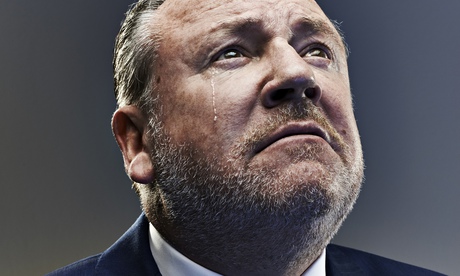 Ray WInstone in a suit and tie with a fake tear on his cheek, looking up