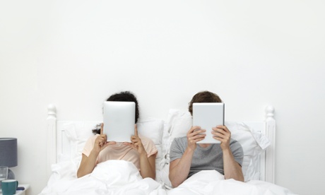 Couple looking at digital tablets in bed