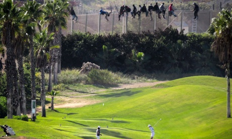 A golfer hits a shot as African migrants sit atop a fence during an attempt to cross into Spanish territories from Morocco.