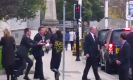 A still image taken from video shows a man approaching Britain's Prime Minister David Cameron as he leaves a news conference in Leeds