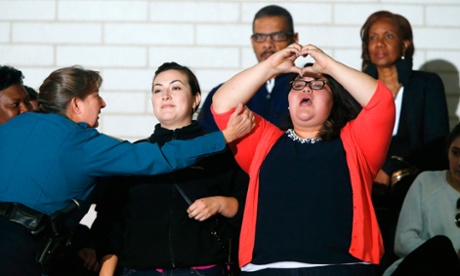 A protestor for immigration reform flashes a heart symbol as she is removed by police for shouting during a speech by Hillary Clinton at the University of Maryland.