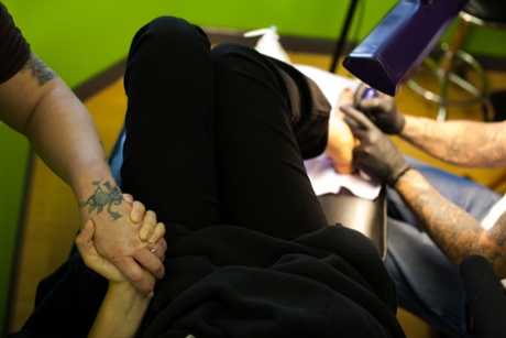 Christina, 29, and Jennifer Kempton, 32, both sex trafficking survivors, hold hands while Charles Waldo covers up Christina's trafficking tattoo with a new tattoo in a tattoo parlour in Lancaster, Ohio, USA. Christina was given a Survivors Ink scholarship by Jennifer Kempton to get her tattoo with the name of her husband and trafficker, covered with artwork.