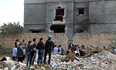 Libyan citizens stand beside a building damaged in the national army's air strikes in Tripoli.