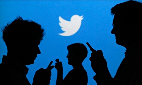 Silhouettes of people on smartphones with Twitter logo in the background
