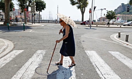 Elderly woman holding an umbrella crosses a street during summer heatwave in Nice, France