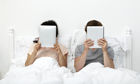 Couple looking at digital tablets in bed