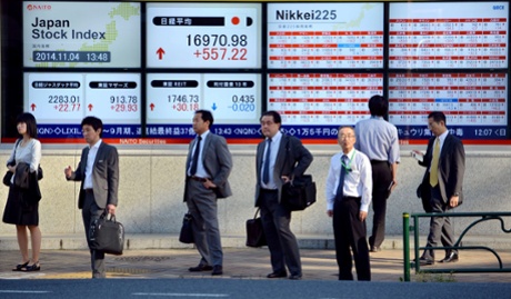 Pedestrians stand in front of stock market boards along the pavement in Tokyo on November 4, 2014.