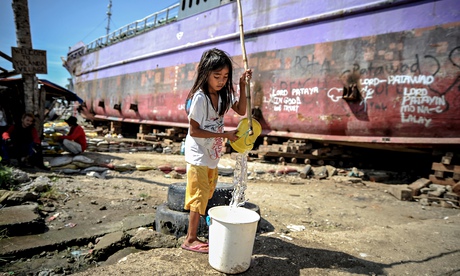 A Filipino girl fills a bucket next to a ship that was washed ashore by typhoon Haiyan in Tacloban