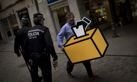 Businessman Emilio Busquets walks past two police officers patrolling the street, as he holds a drawing of a ballot box to decorate his shop.