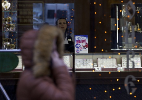 A saleswoman waits for customers in a jewerly shop with a poster reading 