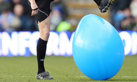 Man about to burst a balloon on a football pitch with his foot